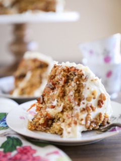 Slice of carrot cake on a plate with carrot cake in the background.