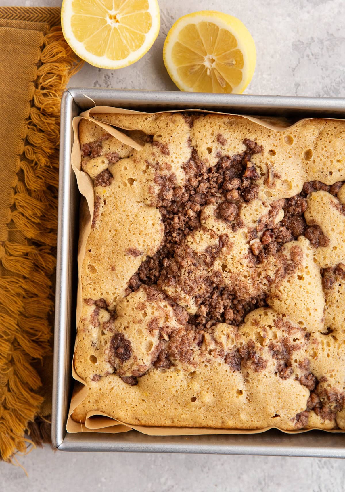 Almond Flour Lemon Coffee Cake in a square pan, fresh out of the oven with lemons to the side.