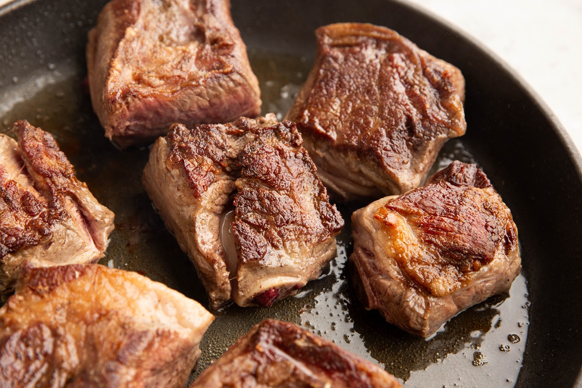 Bone-in beef short ribs searing in a skillet, browned to perfection.