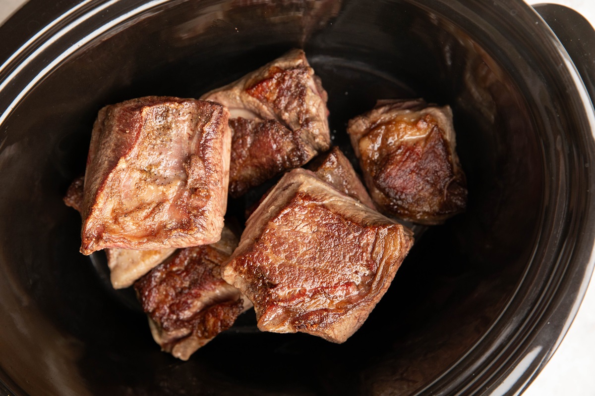 Browned short ribs in the bottom of a crock pot.
