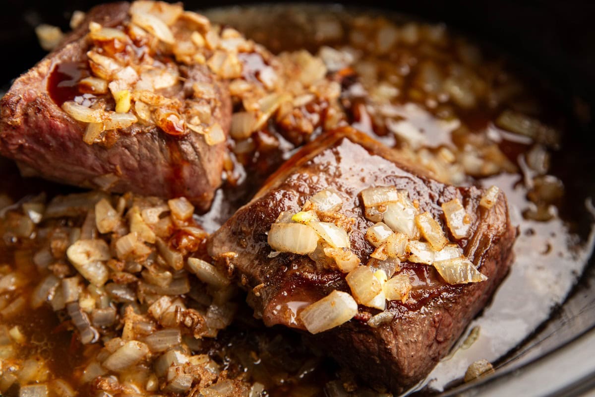 Braising liquid, browned beef ribs and cooked onions in a crock pot, ready to start the slow cooking process.