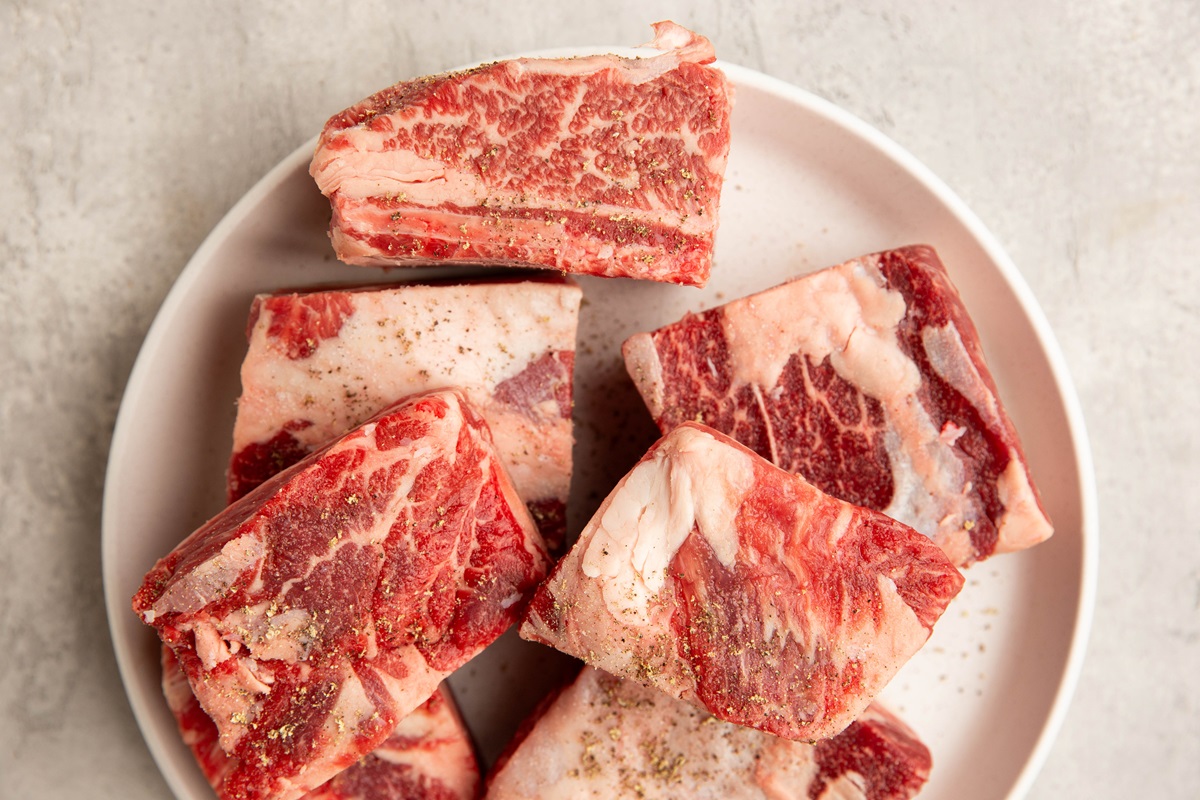 Plate of raw short ribs sprinkled with salt and pepper to make Korean beef short ribs