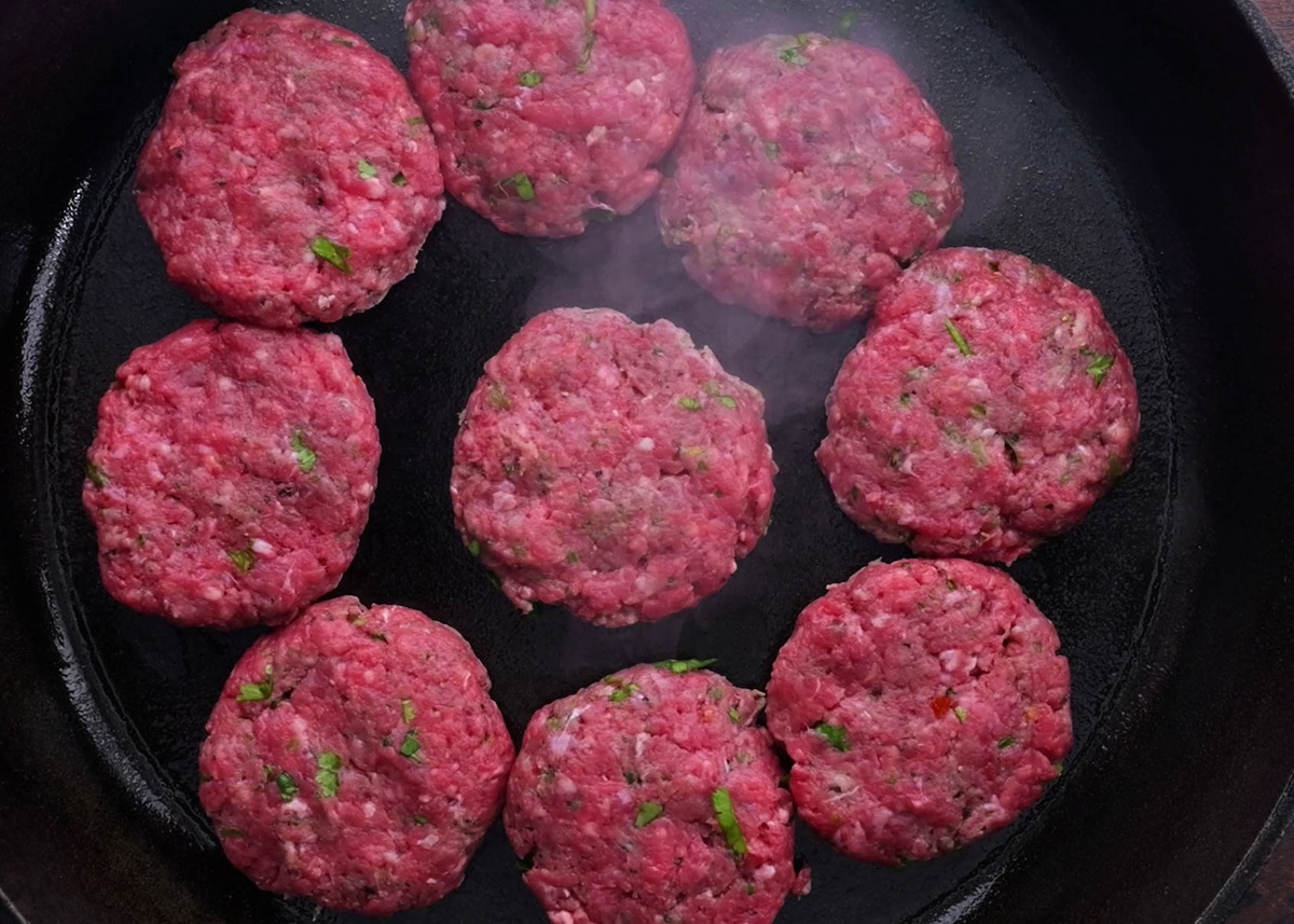 Ground beef sliders cooking on a cast iron skillet.