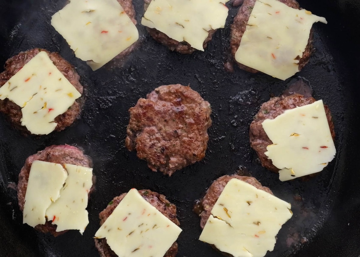 Slices of cheese on top of small hamburger patties in a cast iron skillet