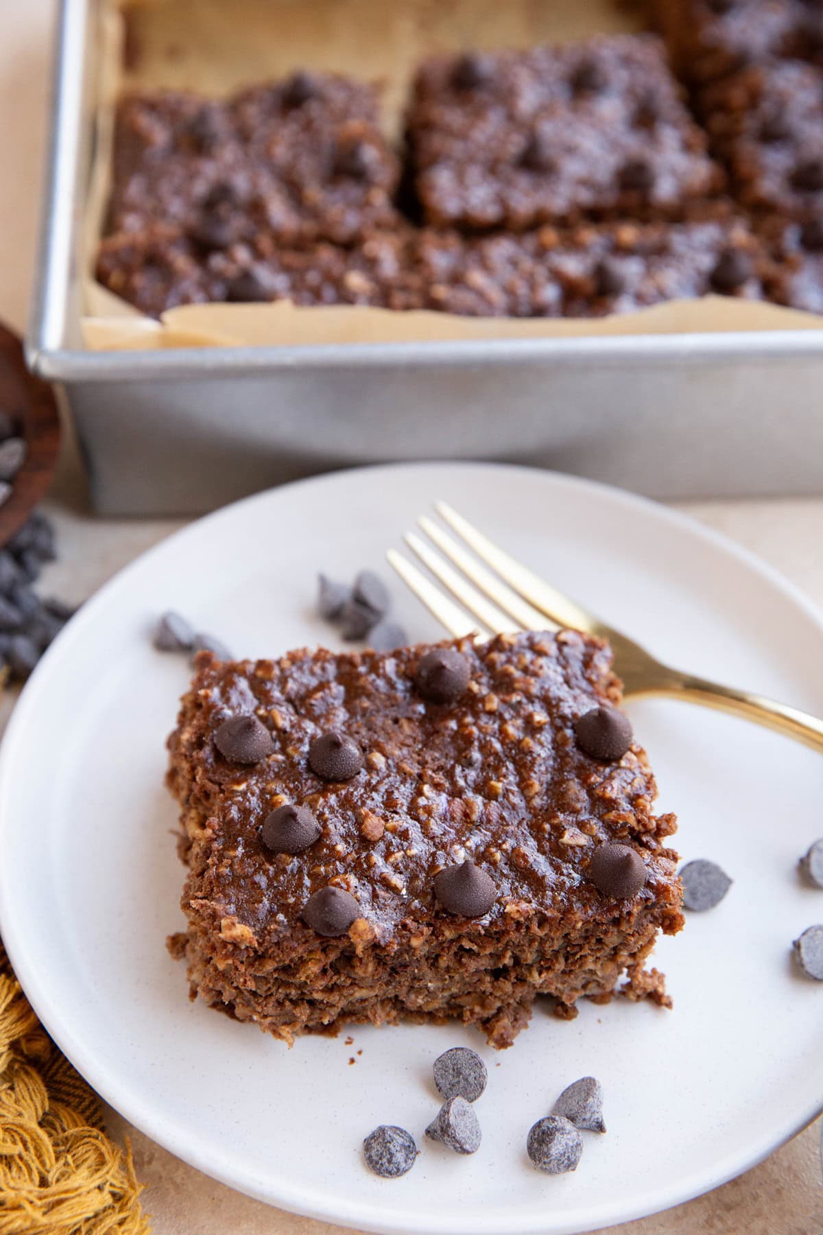 White plate with a slice of chocolate protein oatmeal and the rest of the baked oatmeal in the background.