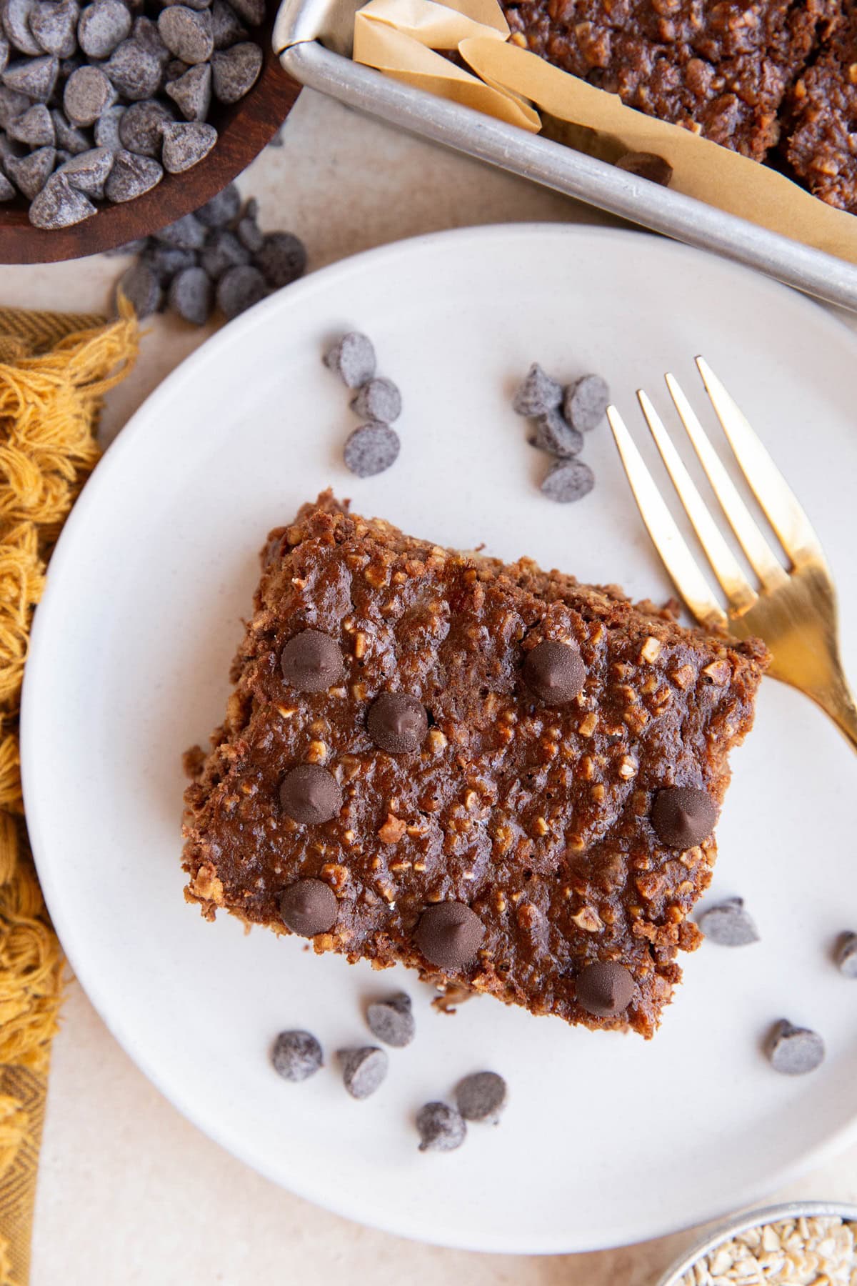 Slice of chocolate banana protein oatmeal on a white plate with a fork and chocolate chips, ready to eat.