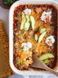 Casserole dish with cheesy ground turkey casserole, topped with sour cream and sliced avocado.