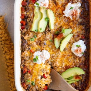 Casserole dish with cheesy ground turkey casserole, topped with sour cream and sliced avocado.