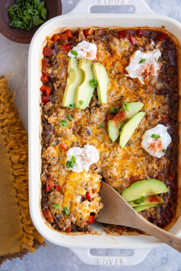 Casserole dish with cheesy ground turkey casserole, topped with sour cream and sliced avocado.
