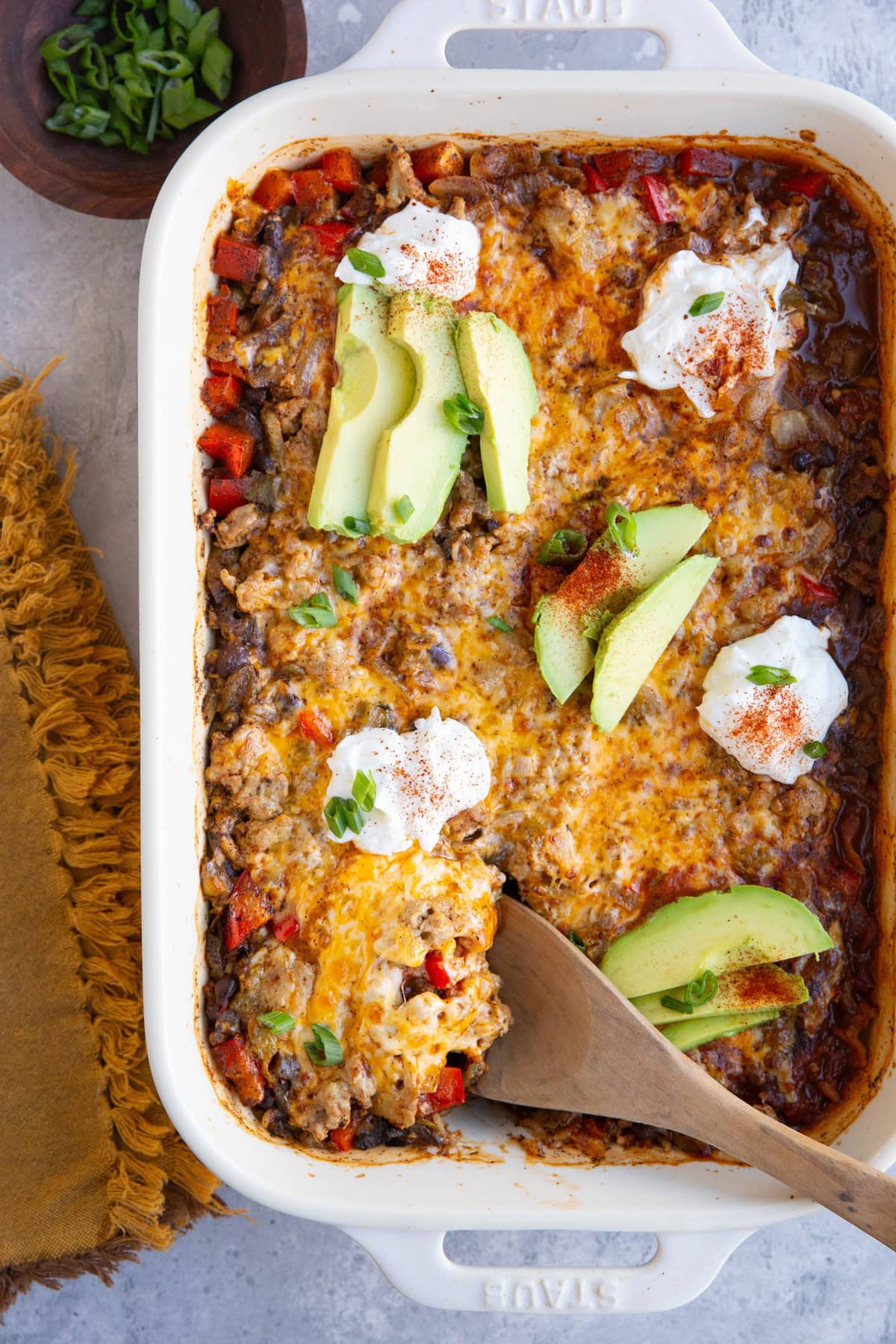 Casserole dish with cheesy ground turkey casserole, topped with sour cream and sliced avocado.