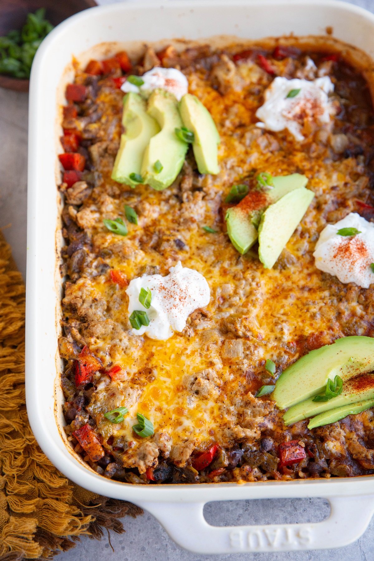 Casserole dish with cheesy turkey taco casserole, topped with slices of avocado and sour cream.