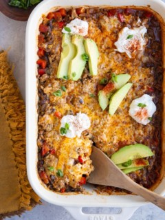 White casserole dish full of cheesy ground turkey casserole with sliced avocado and sour cream on top.