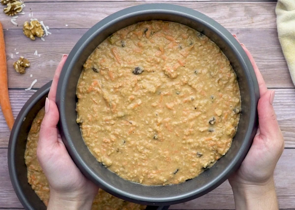 Hand holding a cake pan with carrot cake batter.