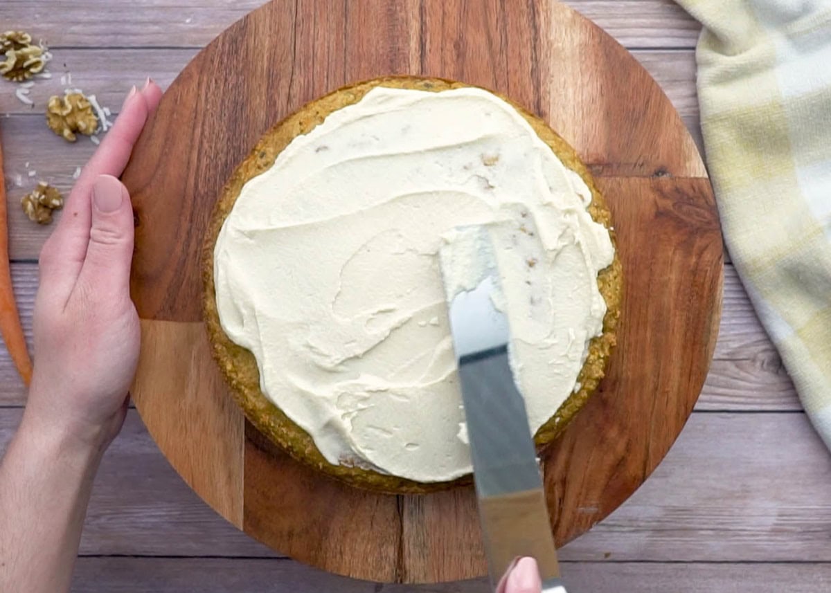 Hand spreading cream cheese frosting over baked carrot cake.