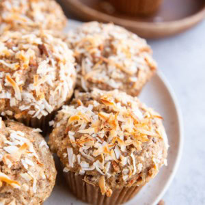 White plate full of carrot cake muffins. A golden napkin to the side and a wooden plate in the background with a muffin on top.