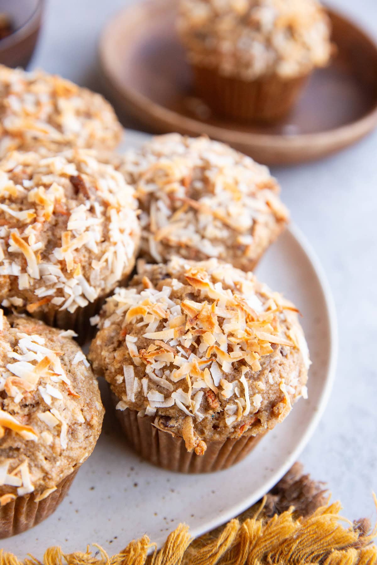 White plate full of carrot cake muffins. A golden napkin to the side and a wooden plate in the background with a muffin on top.