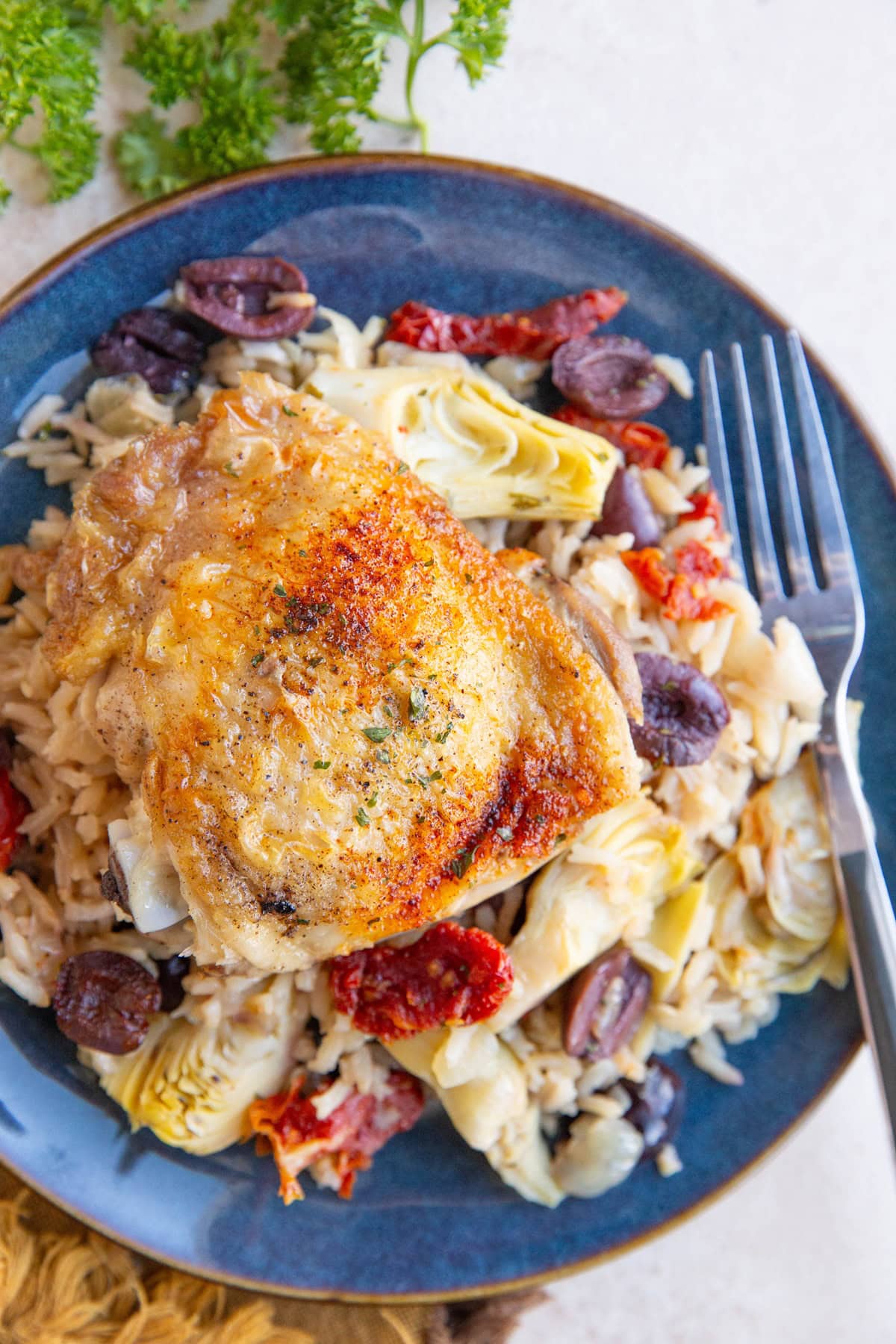 Blue plate with a cooked chicken thigh and Mediterranean rice with a fork and napkin, ready to eat.