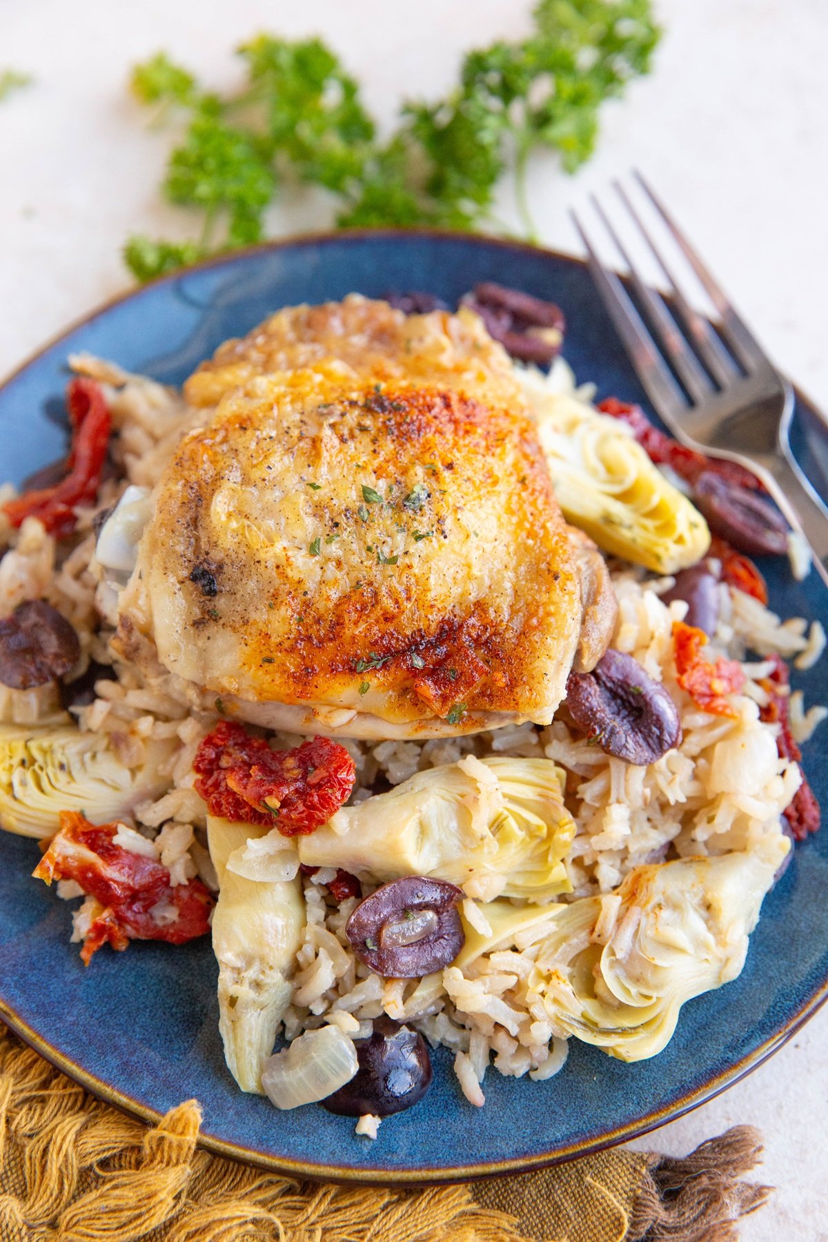 Blue plate of chicken and rice with artichoke hearts, olives, and tomatoes, ready to serve.