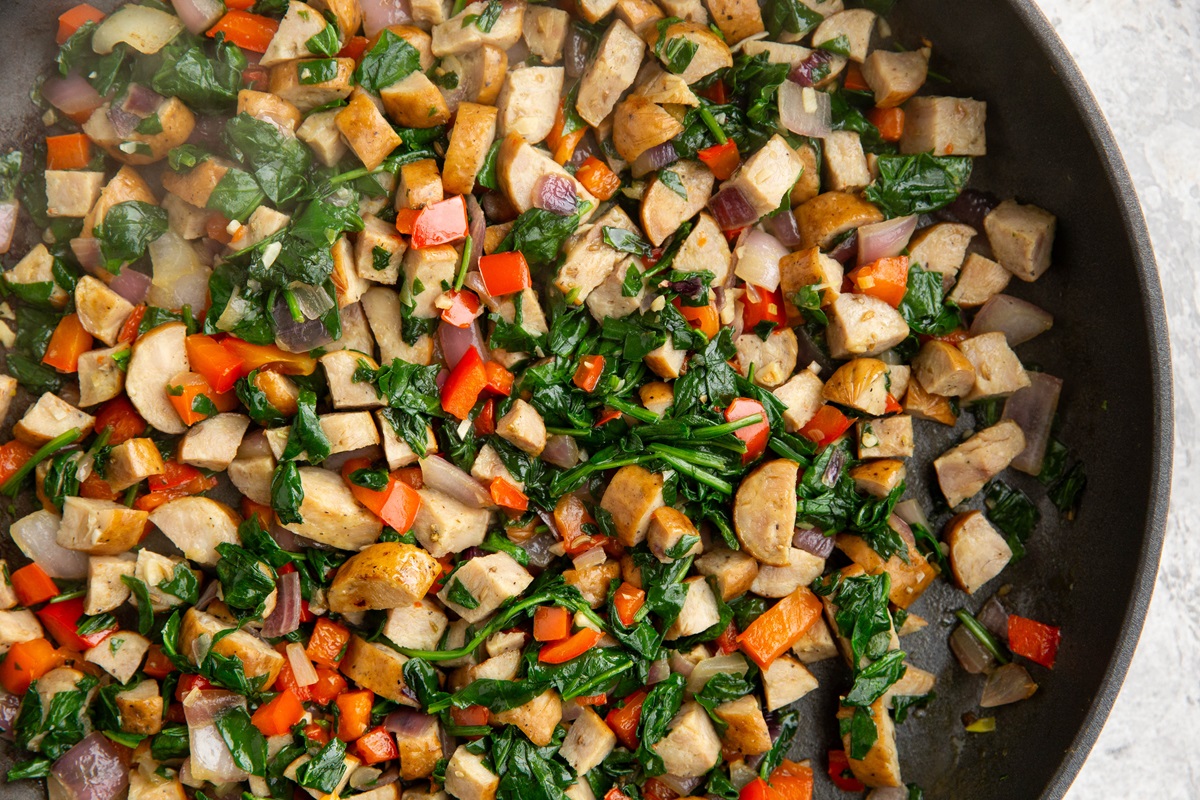 Sausage, bell pepper, onion, and spinach cooking in a skillet.