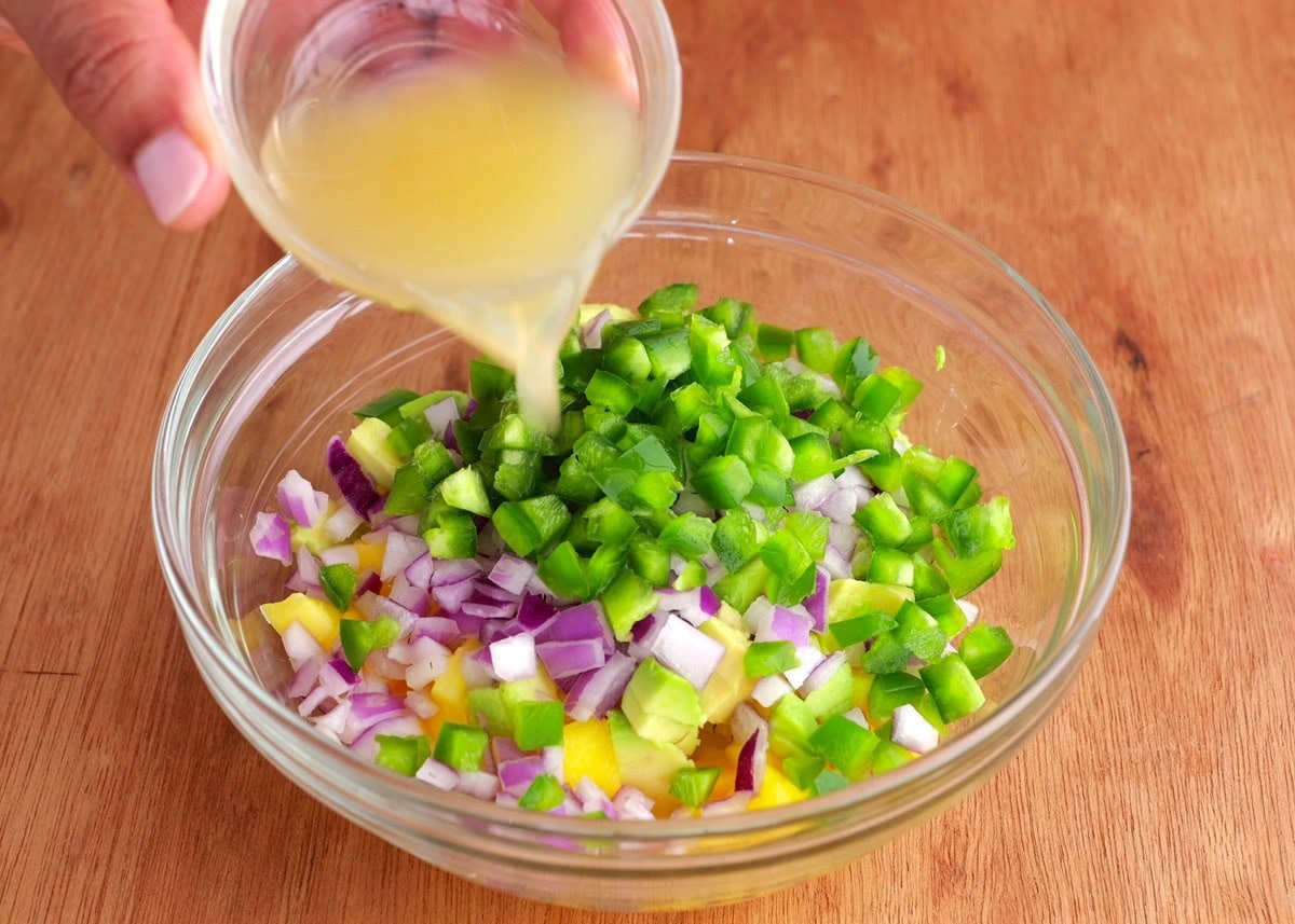 Pouring lime juice into a bowl with mango salsa ingredients.