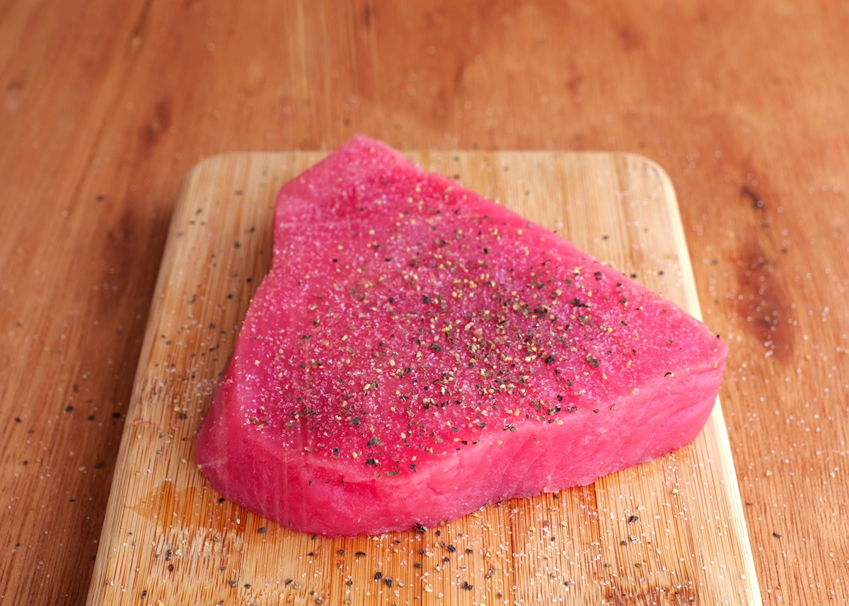 Seasoned ahi steak on a cutting board, ready to sear.