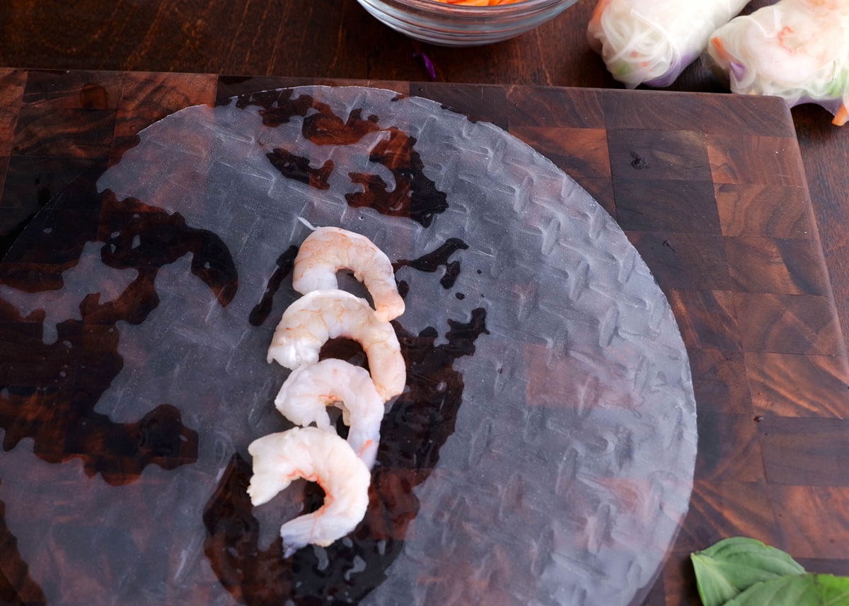 Rice paper on a wooden cutting board with shrimp on top to make spring rolls.