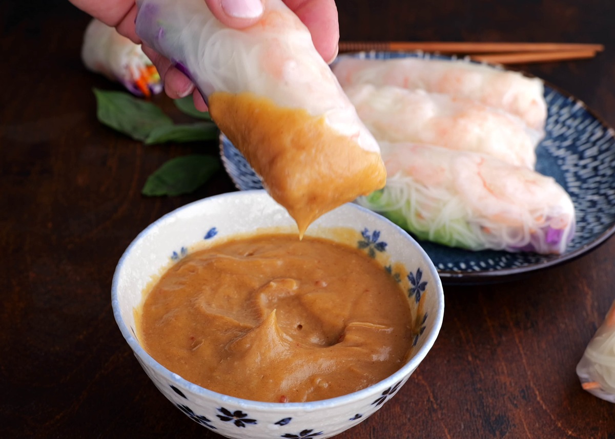 Hand dipping a spring roll into peanut sauce.
