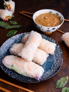 Plate of shrimp spring rolls with bowl of peanut sauce in the background.