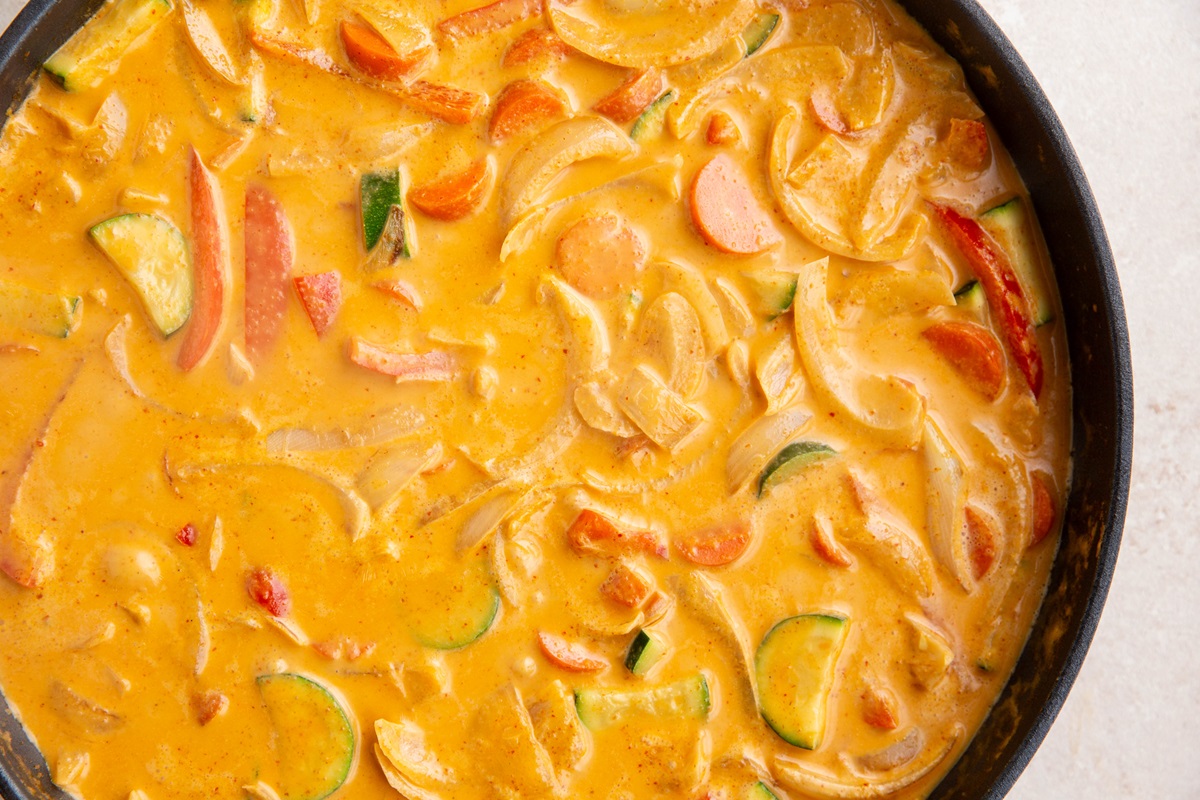Vegetables cooking in red curry sauce in a skillet.