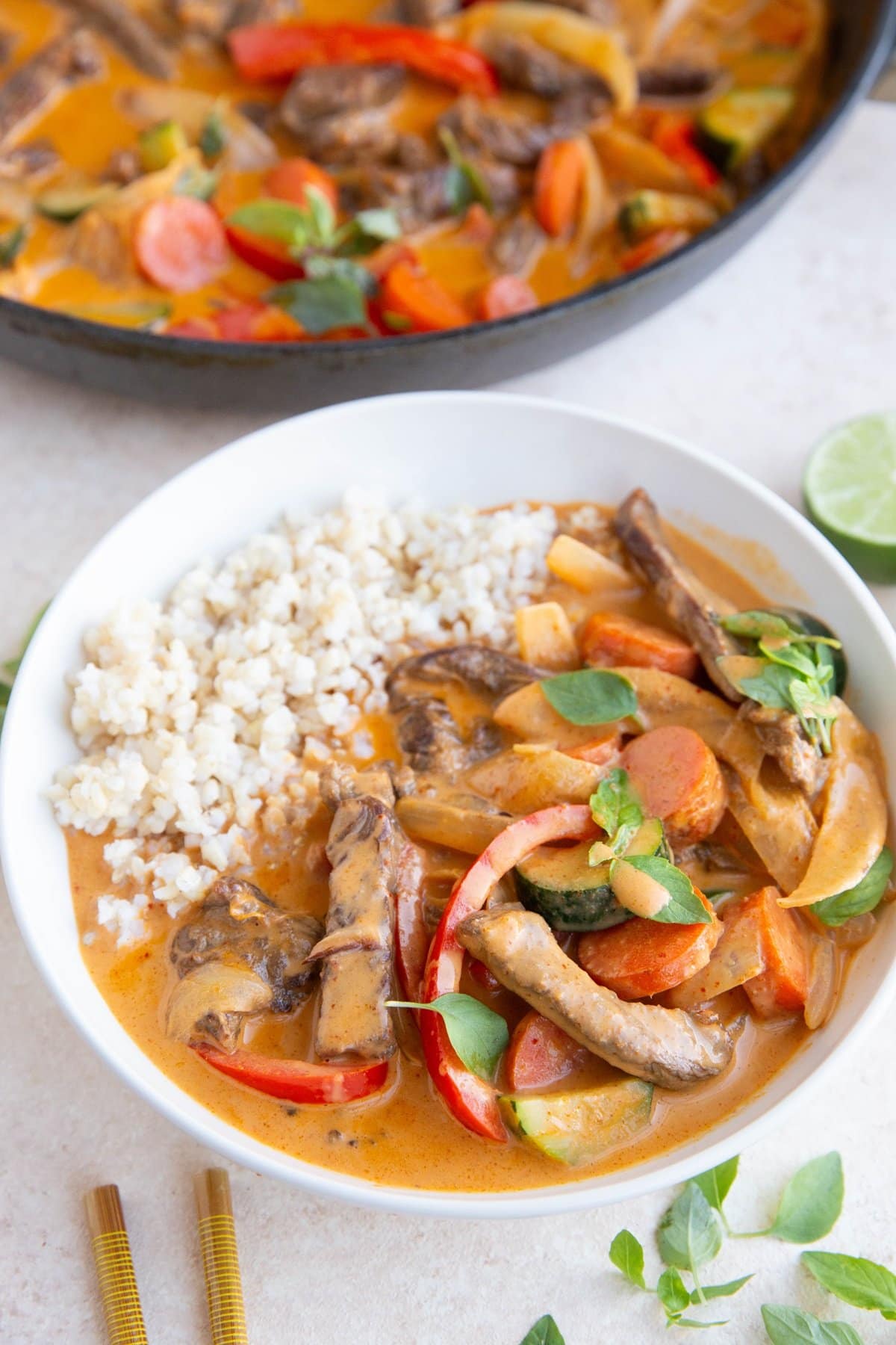 Bowl of beef curry with brown rice and more beef curry in the background.