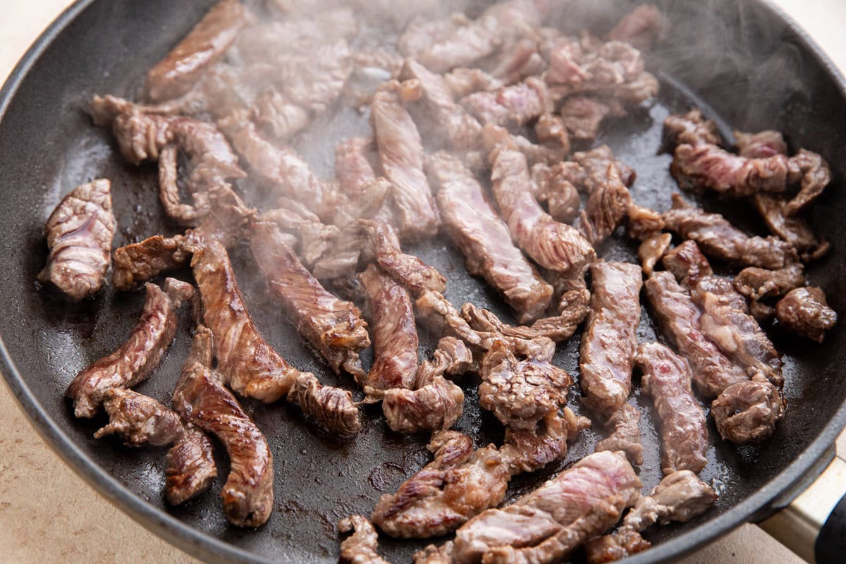 Strips of steak browning in a skillet.