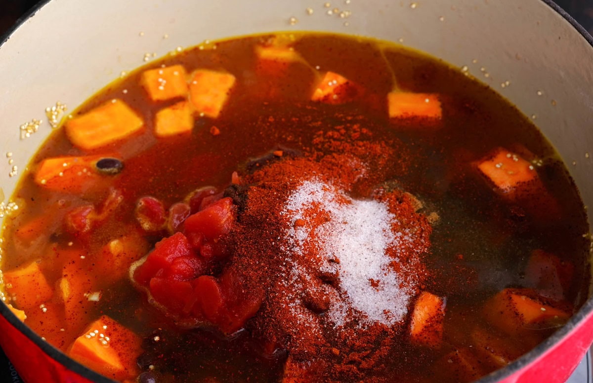 Sweet potato quinoa chili with broth and seasonings added in, ready to stir.