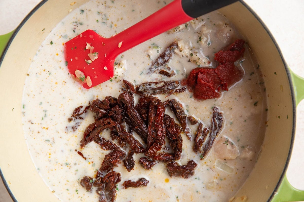 Large soup pot with chicken, onion, creamy sauce, sun-dried tomatoes and tomato paste, ready to be stirred together.