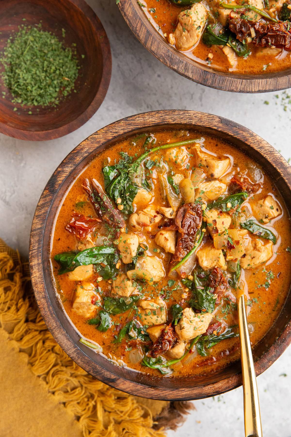 Two wooden bowls full of Tuscan soup with a gold spoon and a gold napkin, ready to serve.