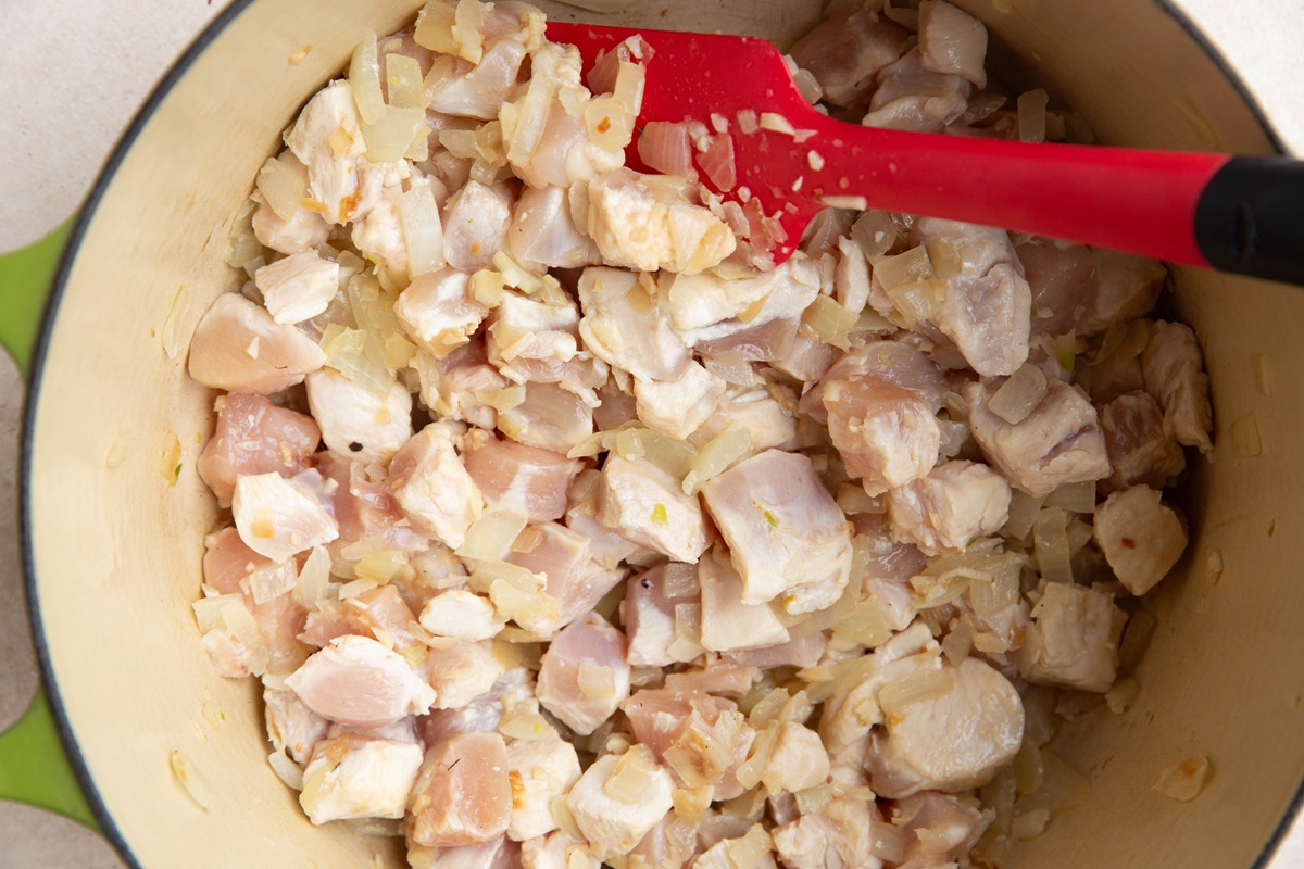 Onion and chopped chicken breasts cooking in a large pot to make soup.