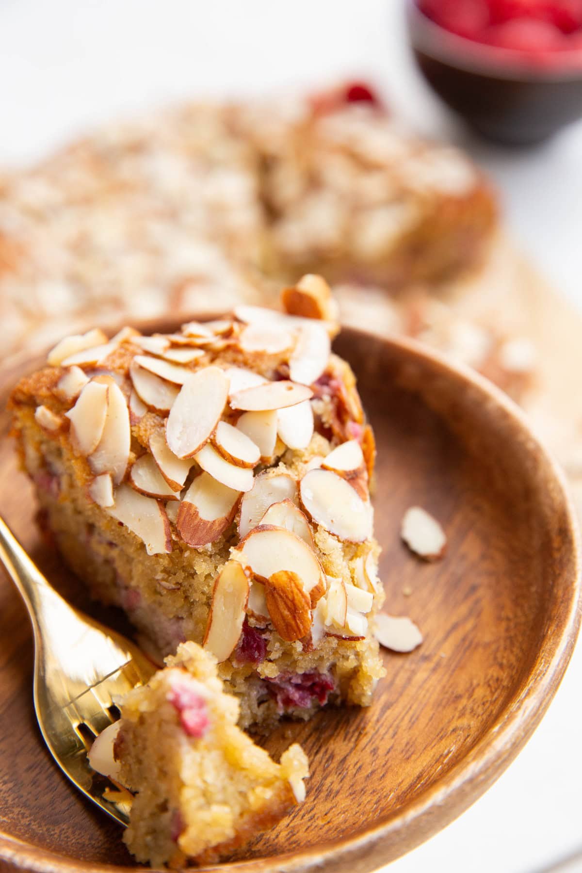 Slice of almond flour raspberry cake on a wooden plate with a bite taken out.