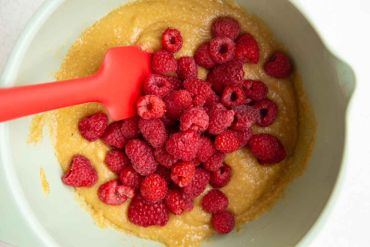 Mixing bowl with cake batter inside with fresh raspberries on top.