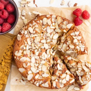 Raspberry almond cake on a white background with three slices cut. Fresh raspberries and sliced almonds all around.