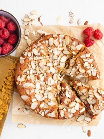 Raspberry almond cake on a white background with three slices cut. Fresh raspberries and sliced almonds all around.