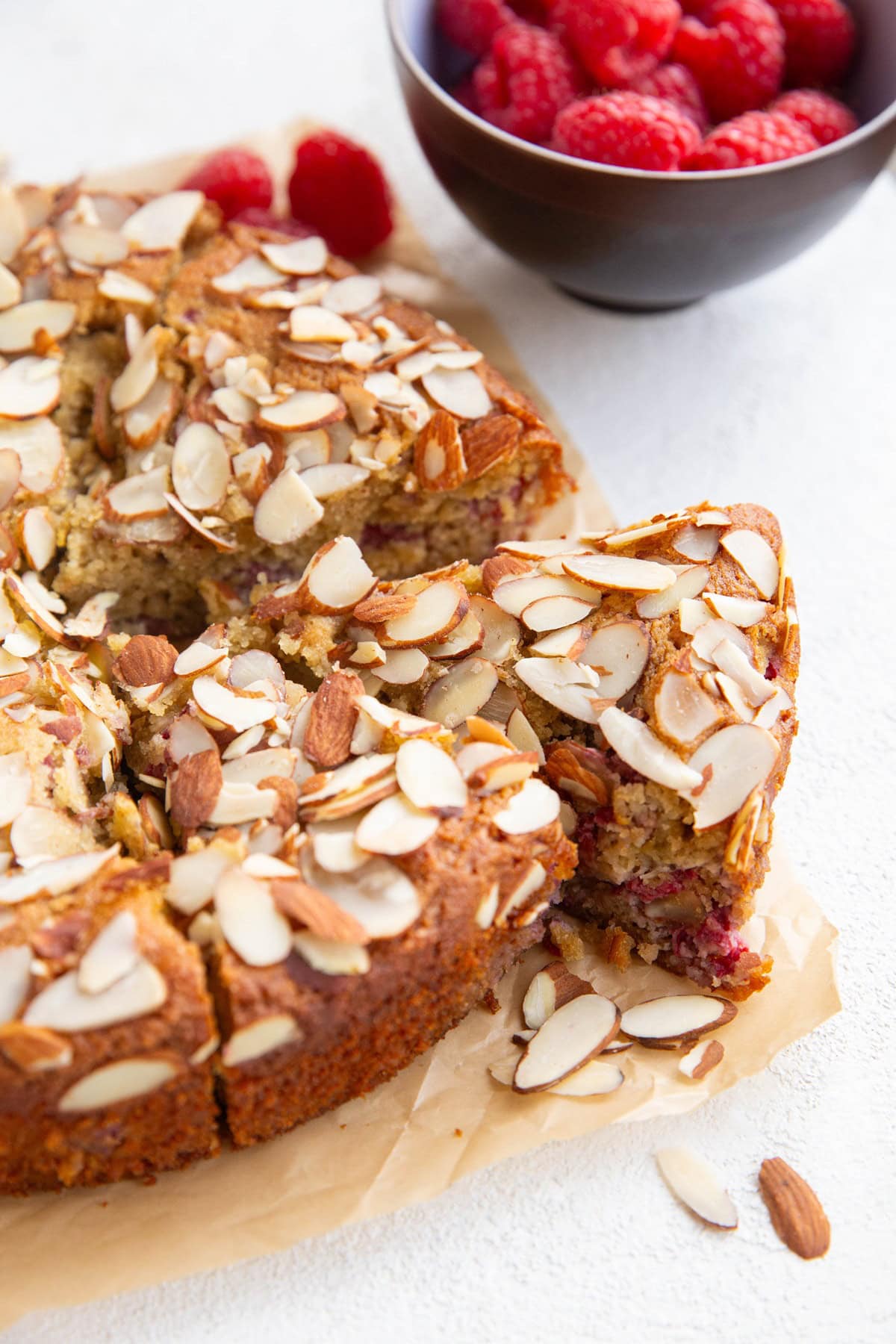 Almond flour raspberry cake cut into slices with one slice poking out.