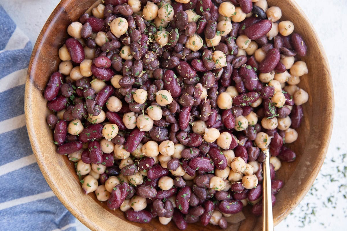 Wooden bowl full of bean salad with a gold spoon, ready to serve.