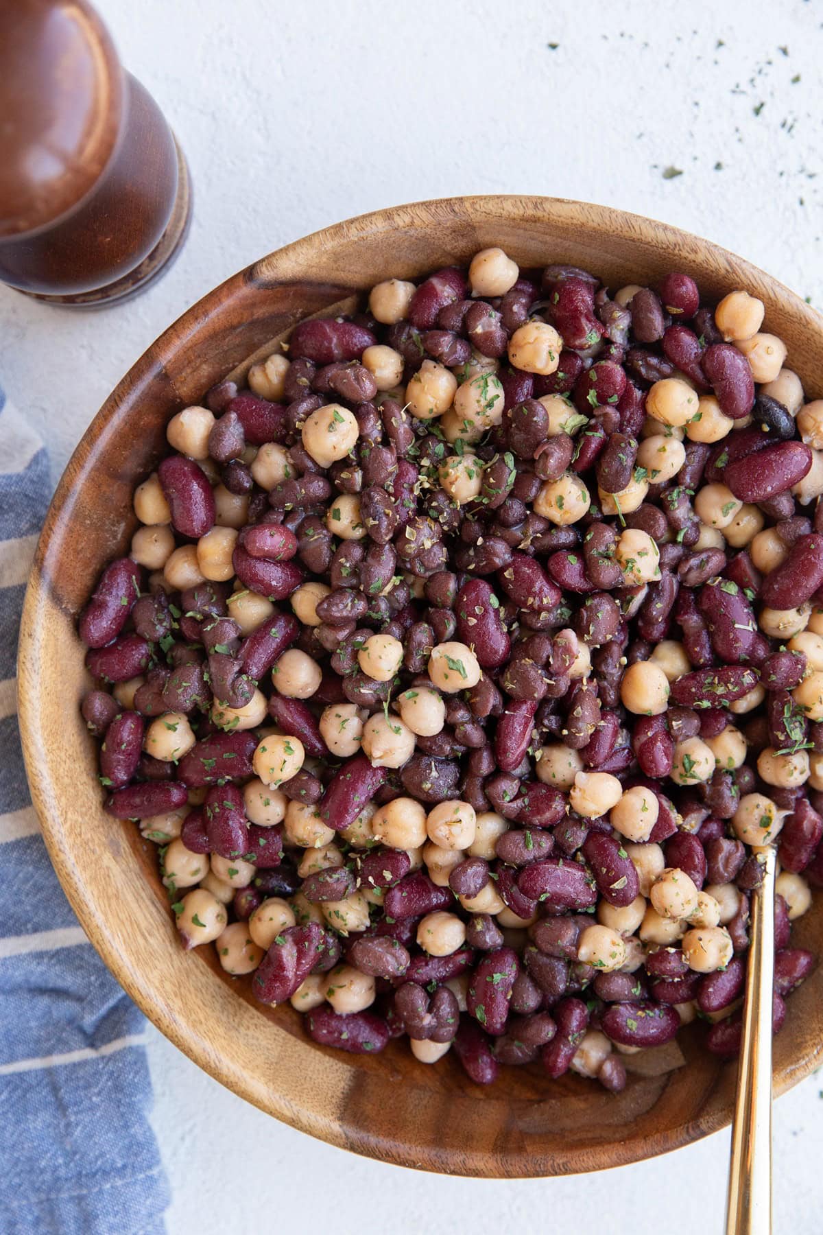 Wooden bowl full of three bean salad sprinkled with parsley, ready to serve.