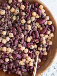 Wooden bowl full of bean salad with a golden spoon, ready to serve for dinner.