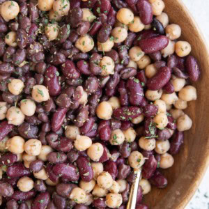 Wooden bowl full of bean salad with a golden spoon, ready to serve for dinner.