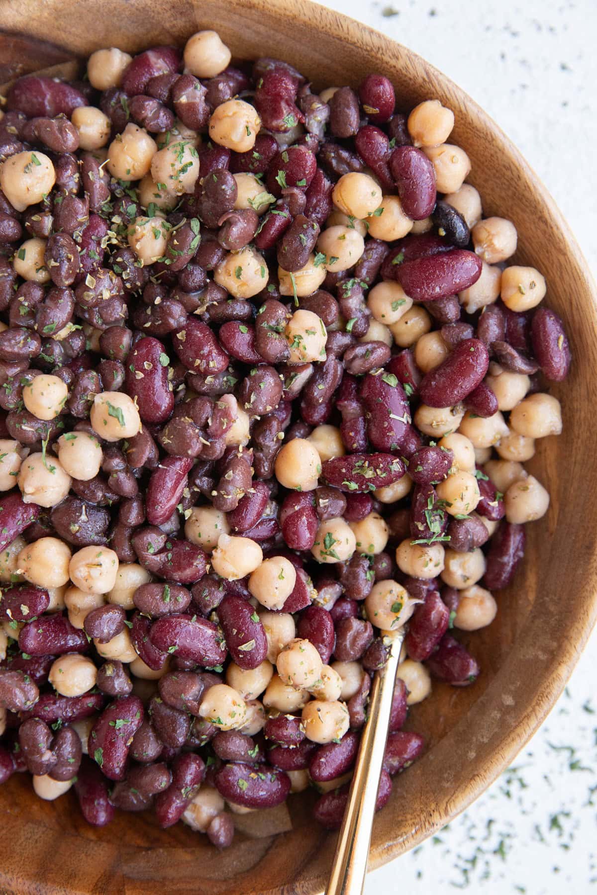 Wooden bowl full of bean salad with a golden spoon, ready to serve for dinner.