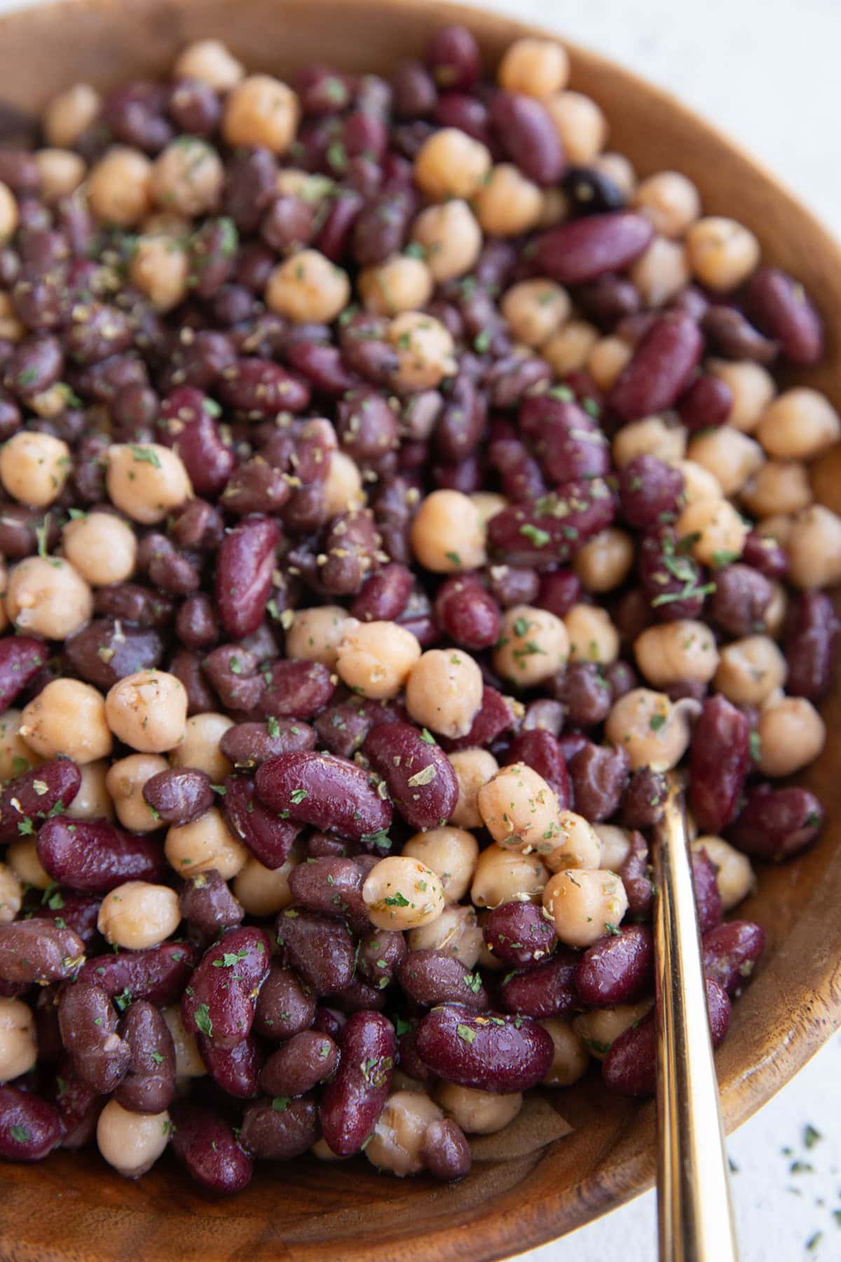 Serving bowl with bean salad inside and a golden spoon for serving.