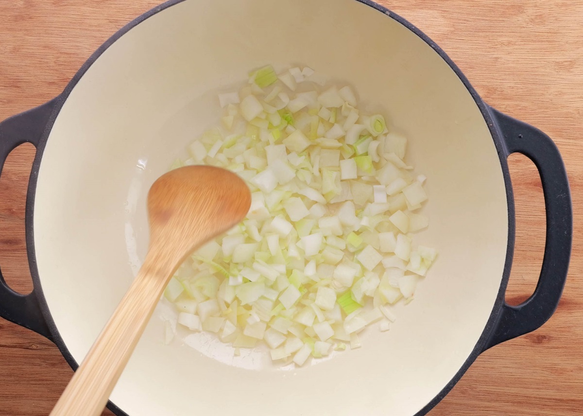 Large pot with chopped onion inside and a wooden spoon stirring the onion.
