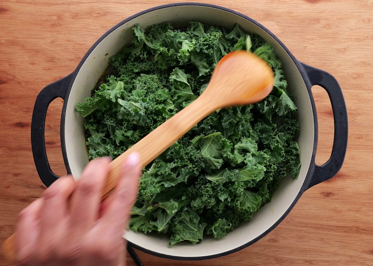 Large pot with chopped kale being stirred into the soup.
