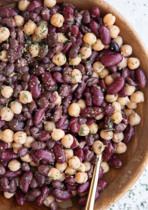 Wooden bowl full of bean salad with a golden spoon, ready to serve for dinner.