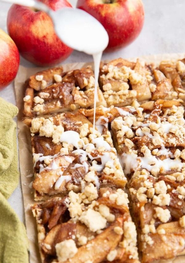 Spoon drizzling glaze over sliced apple crumb bars.